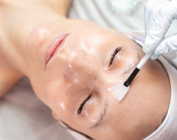 Close-up beautician doctor hand making anti-age procedure apply peeling acid young attractive female client at beauty clinic. Cosmetologist specialist doing skincare treatment. Health care therapy.