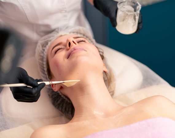 cosmetologist in gloves applies a mask to the client's décolleté and neck with brush skin care